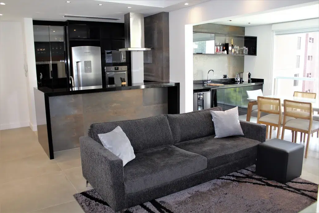 Cozinha americana, sala de estar e mesa de jantar em um mesmo ambiente de um apartamento, estilo industrial com cores sóbrios como preto, café e branco.