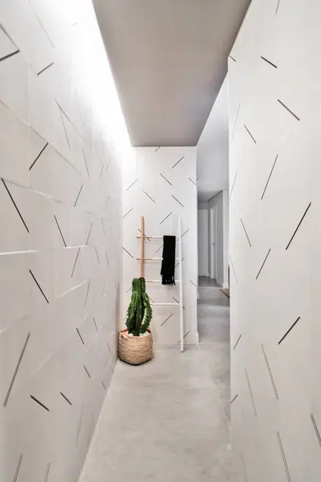 Hall feito de paredes com ladrilhos hidráulicos brancos. Tem um cactus como planta decorativa e iluminação nos cantos do teto.