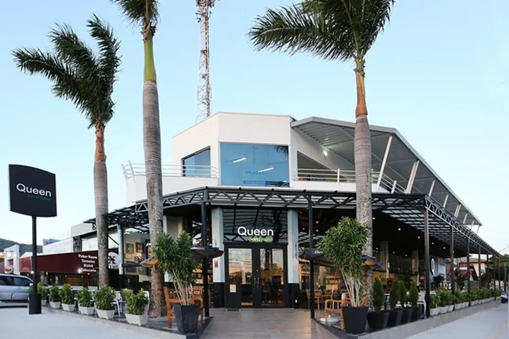 Fachada do restaurante Queen Oceânico, estrutura metálica y estilo moderno com decoração de vasos brancos e pretos com plantas e coqueiros altos.