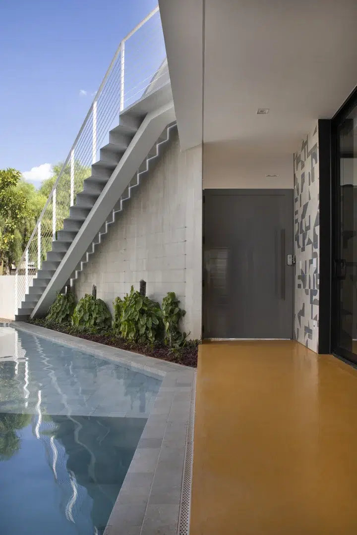 Área externa de uma casa com piscina conectada com a área interna através de uma escada.