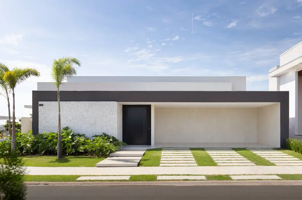 Fachada de uma casa simples de cor branca com a porta preta e um coqueiro.
