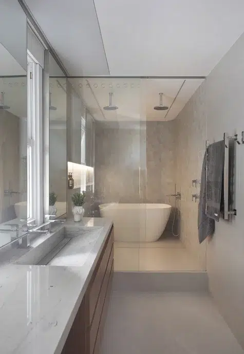 Banheiro em porcelanato natural com uma pia vertical, espelho, uma banheira branca e toalhas penduradas na parede. 