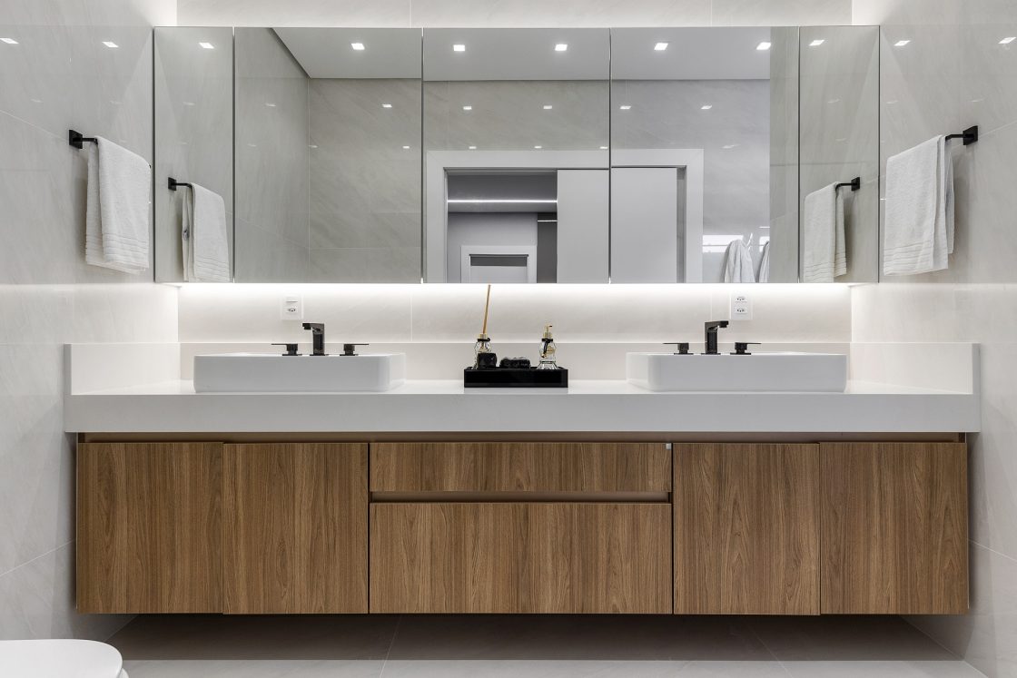 Banheiro de casal com parede marmorizada e gabinete de madeira