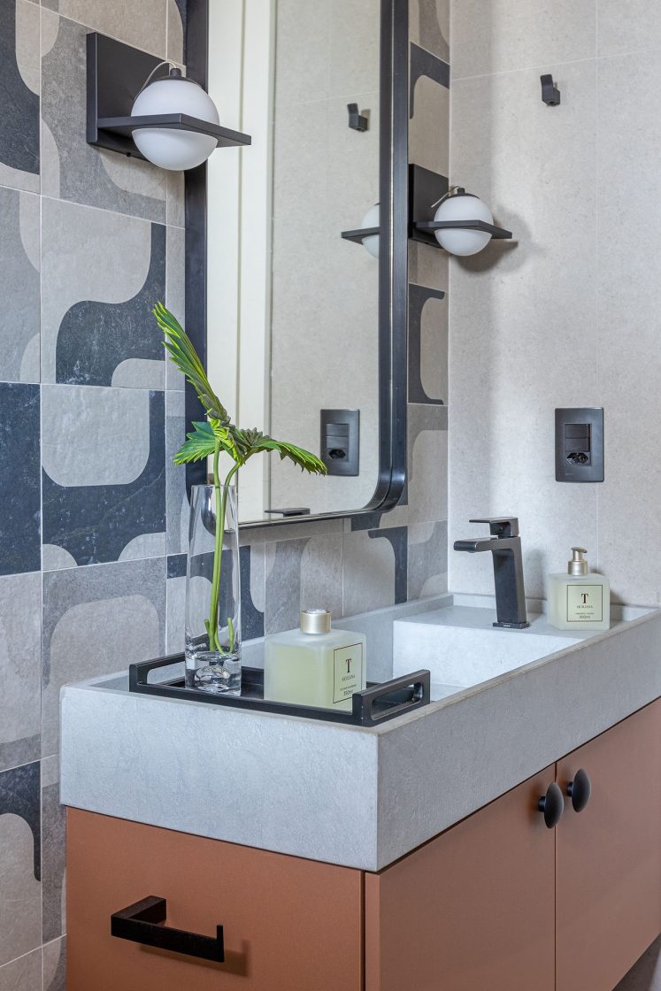 Banheiro charmoso com revestimentos que reproduzem o calçadão de Ipanema nas paredes e marcenaria laranja