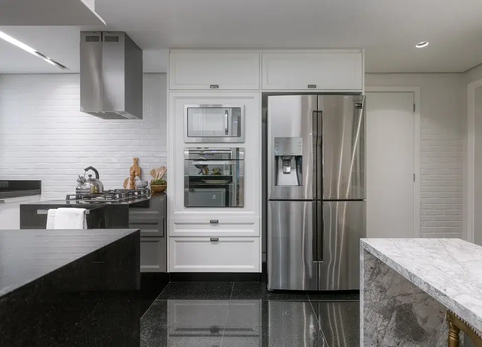 Cozinha com revestimento em porcelanato, eletrodomésticos e moveis nas cores branca, preta e cinza. 