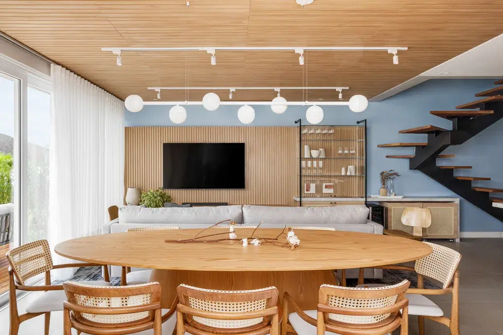 Sala com revestimento amadeirado na parede que combina com a mesa de jantar. Luzes de bolhas brancas no teto.