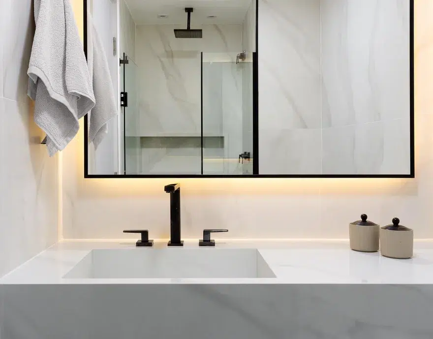 banheiro de luxo com detalhes metalizados no quadro do espelho e na torneira.