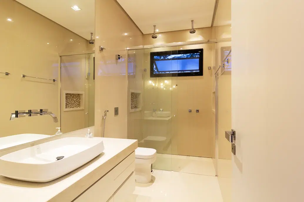 Banheiro clean e minimalista, com dois chuveiros e revestimento em mineral nude e mix corten.