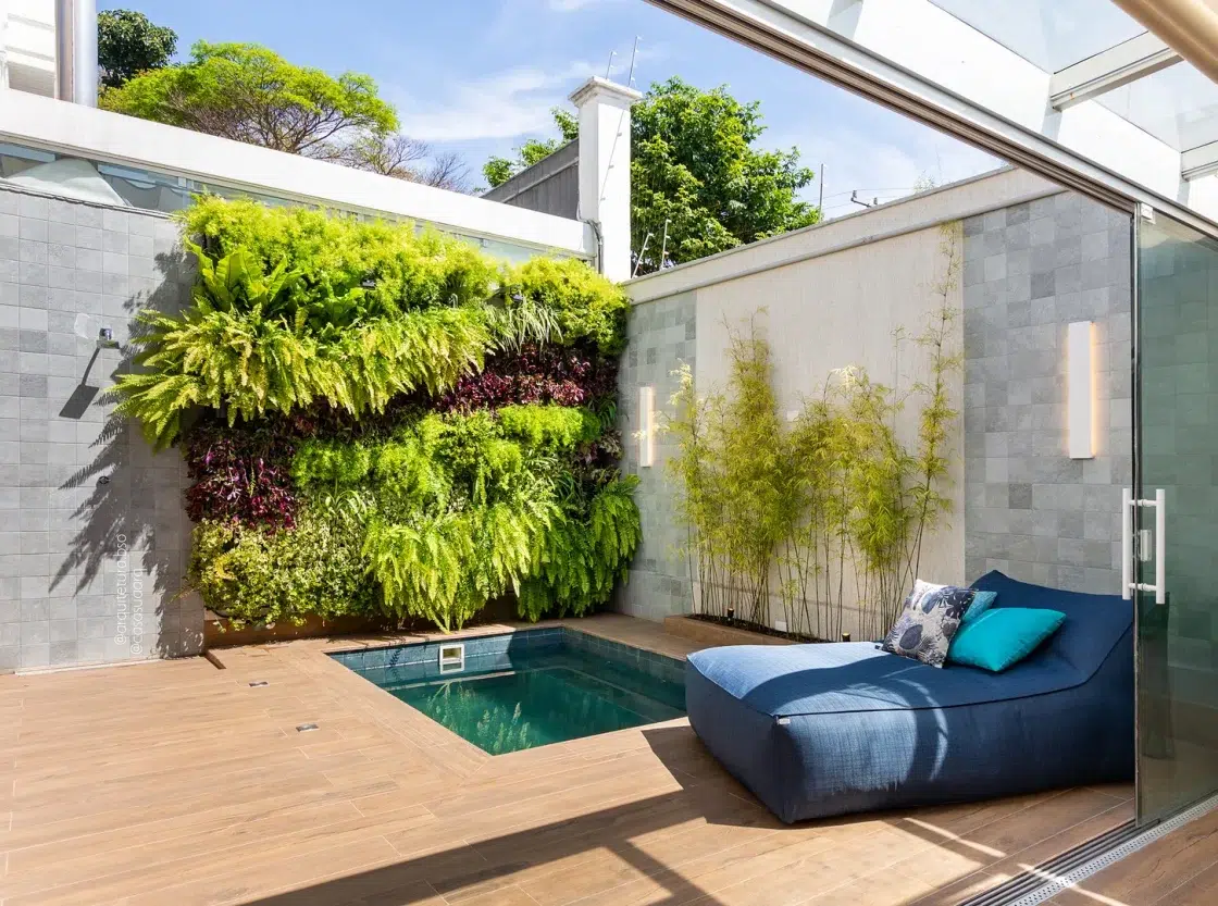 Área externa com ofurô quadrado, sofá azul e jardim vertical ao fundo.