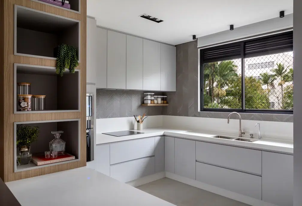 Cozinha branca com meia parede cinza, janela e luz natural.