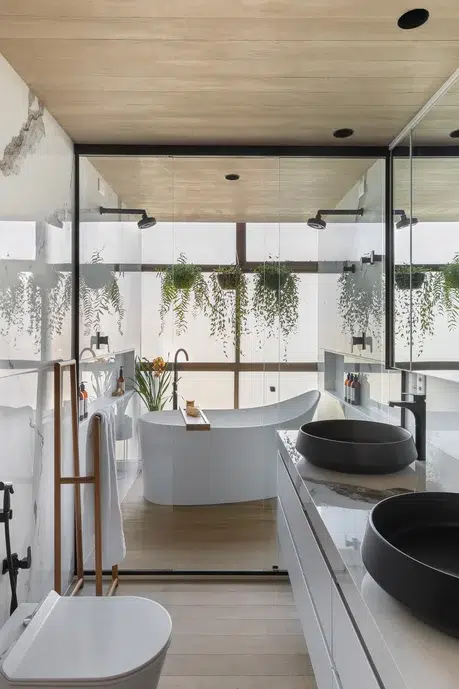 Banheiro de luxo com duas cubas e uma banheira com decoração de plantas penduradas e dois chuveiros.