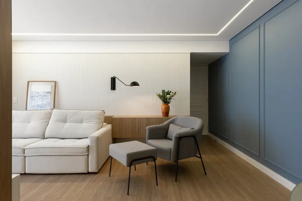 Sala de estar com revestimento imitando madeira no piso, poltrona cinza e sofá off-white.