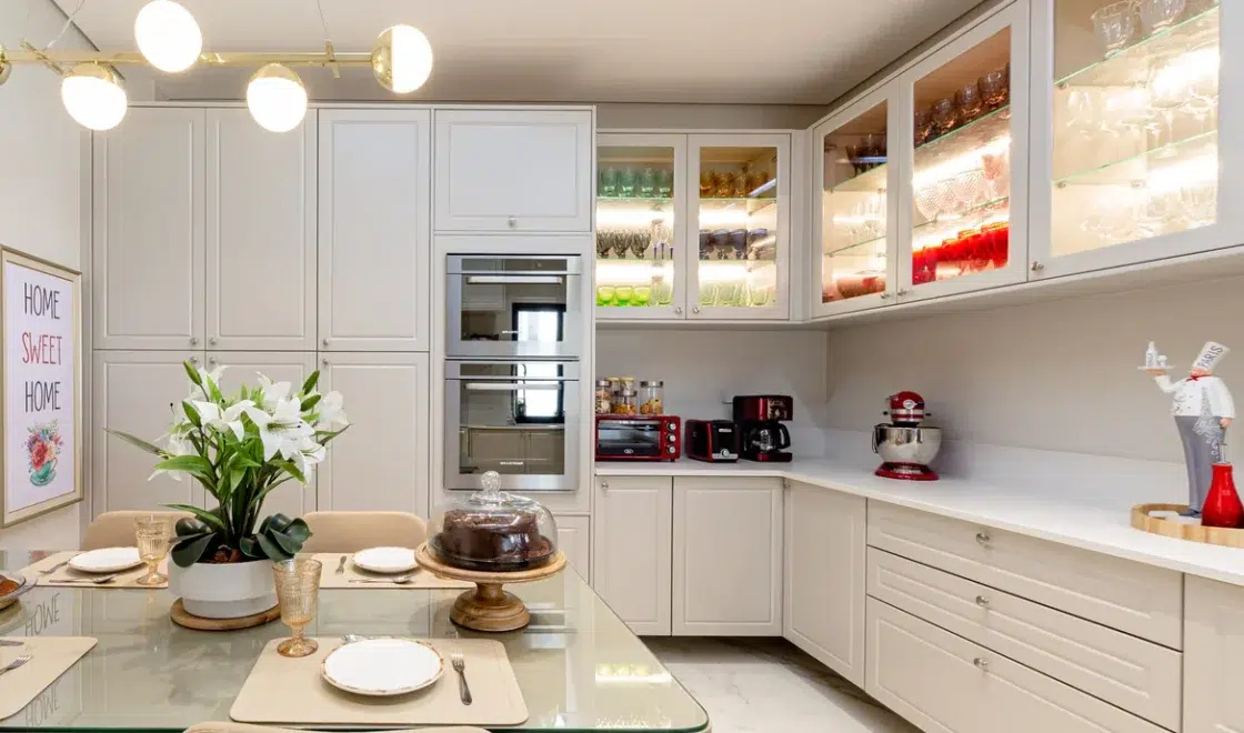 Cozinha estilo provençal com móveis grandes e brancos, com vidro que deixam ver as taças e copos.
