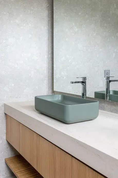 Banheiro com paredes em porcelanato, pietra lonbarda off white, limestone na bancada e madeira carvalho. Cuba de cor verde.