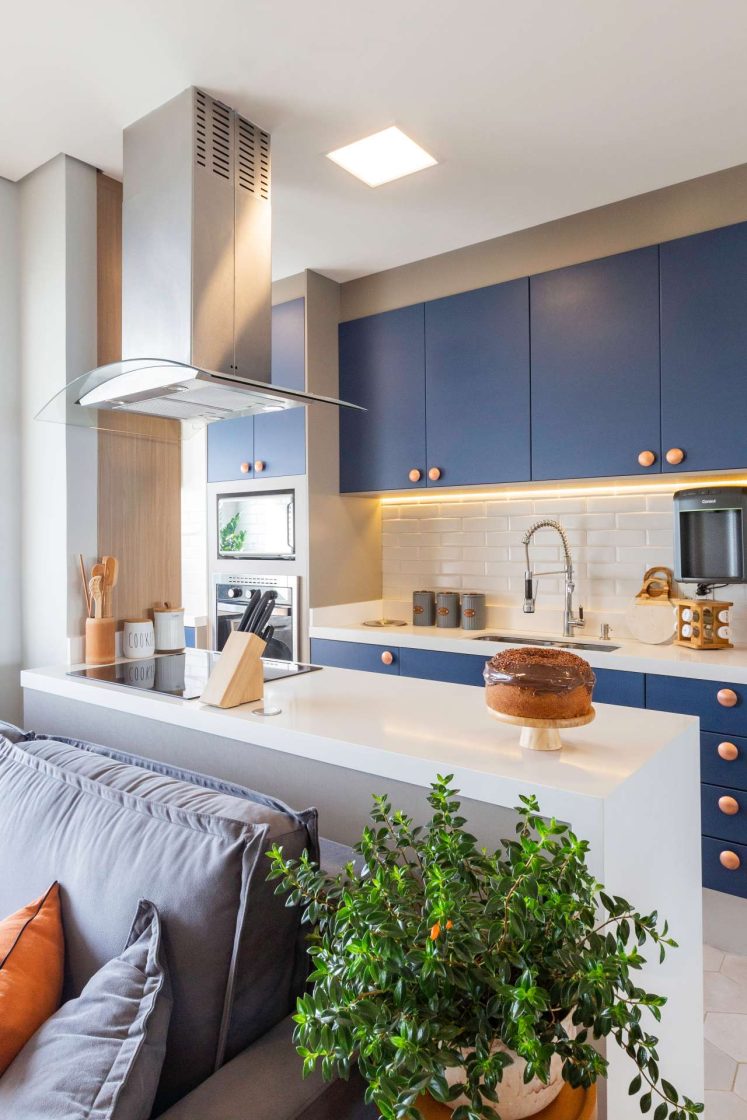 Cozinha integrada com marcenaria azul, backsplash de azulejo tipo metrô e bancadas brancas