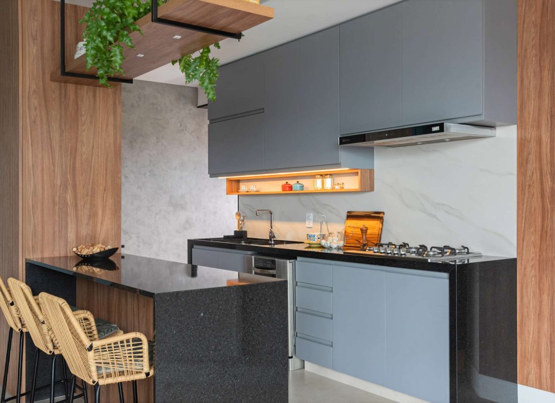 Cozinha integrada com marcenaria azul e em madeira, backsplash marmorizado e bancadas pretas