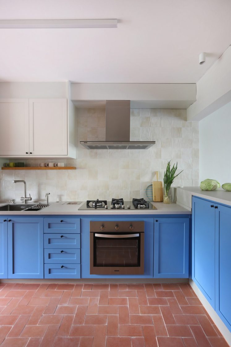 Cozinha ampla, com piso alaranjado, marcenaria azul e backsplash claro