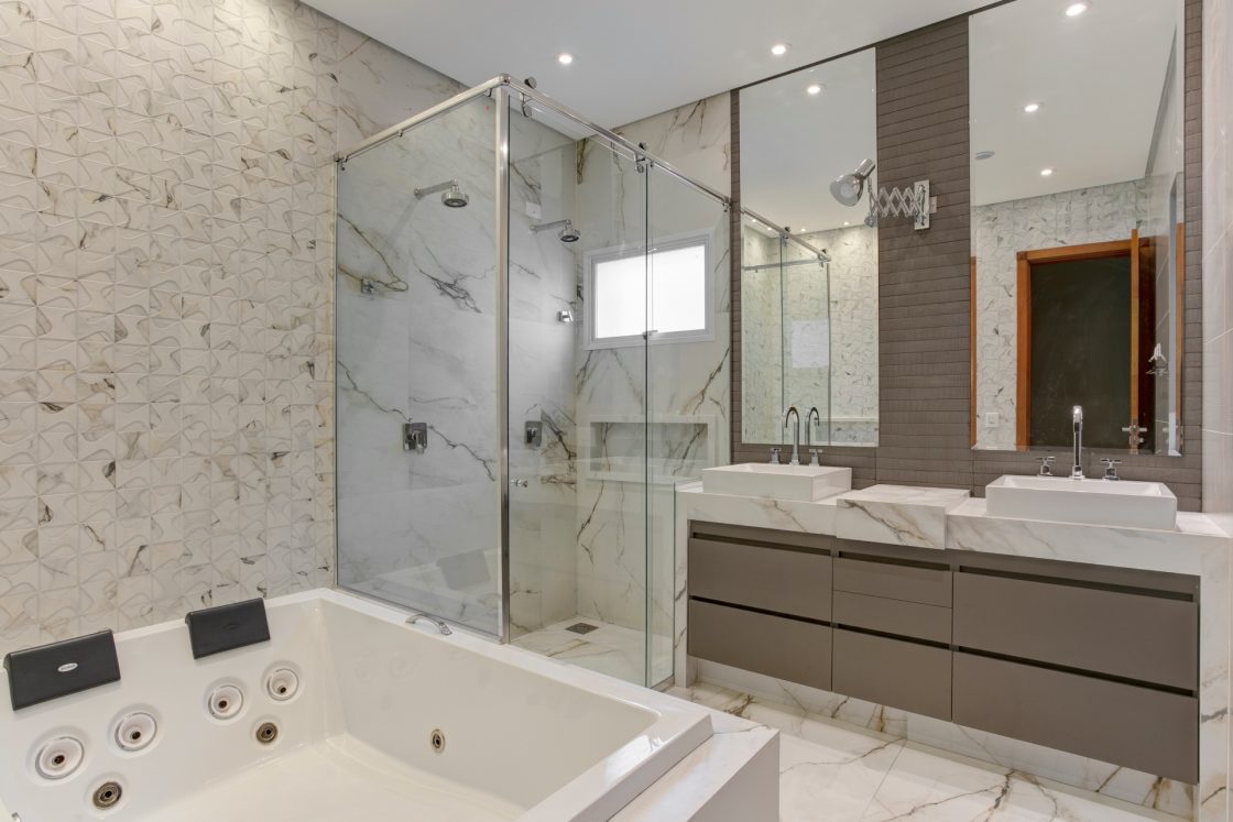 Banheiro com revestimento inspirado em mármore; pia dupla e chuveiro duplo
