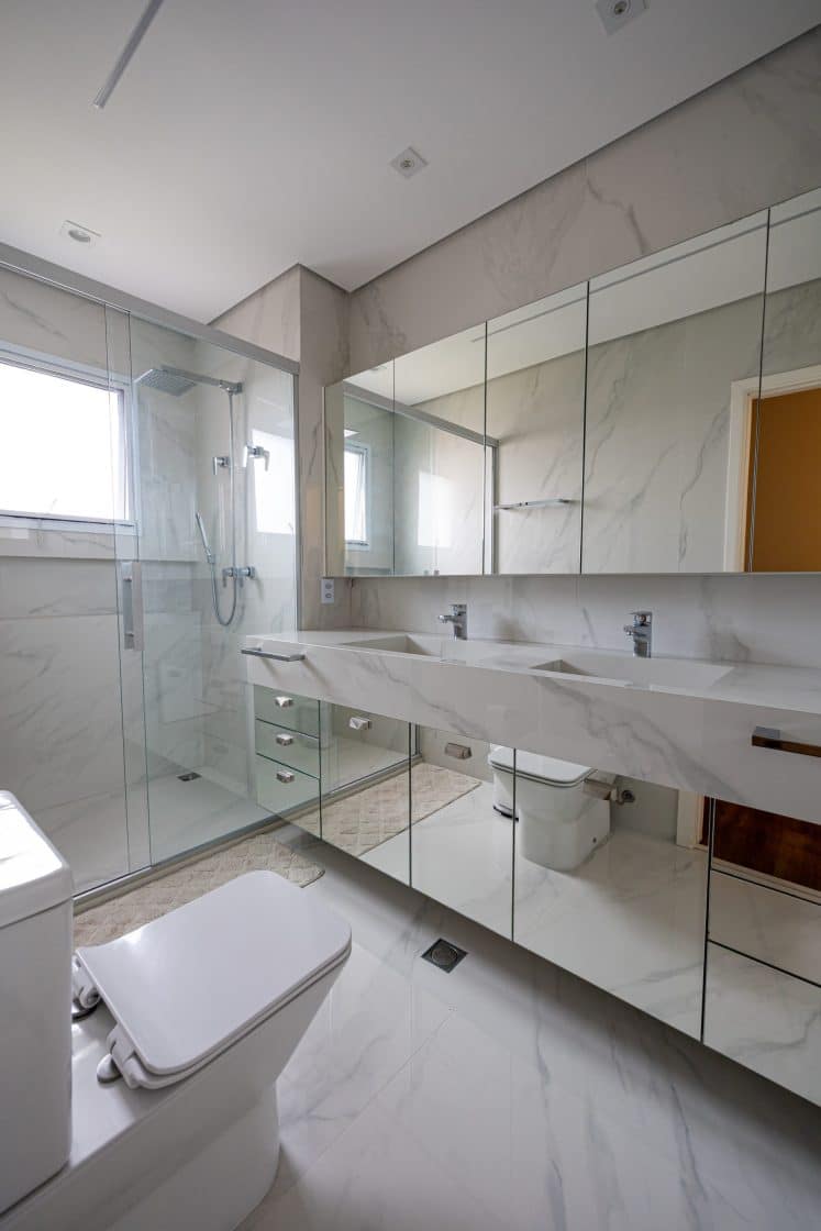 banheiro de suíte com revestimento marmorizado, armários espelhados 