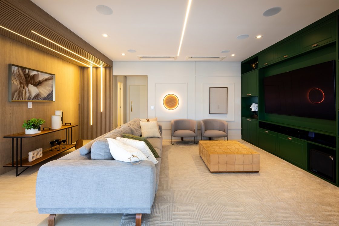 sala de estar com parede verde folha, sofá cinza, pufe creme, e luminárias embutidas no teto