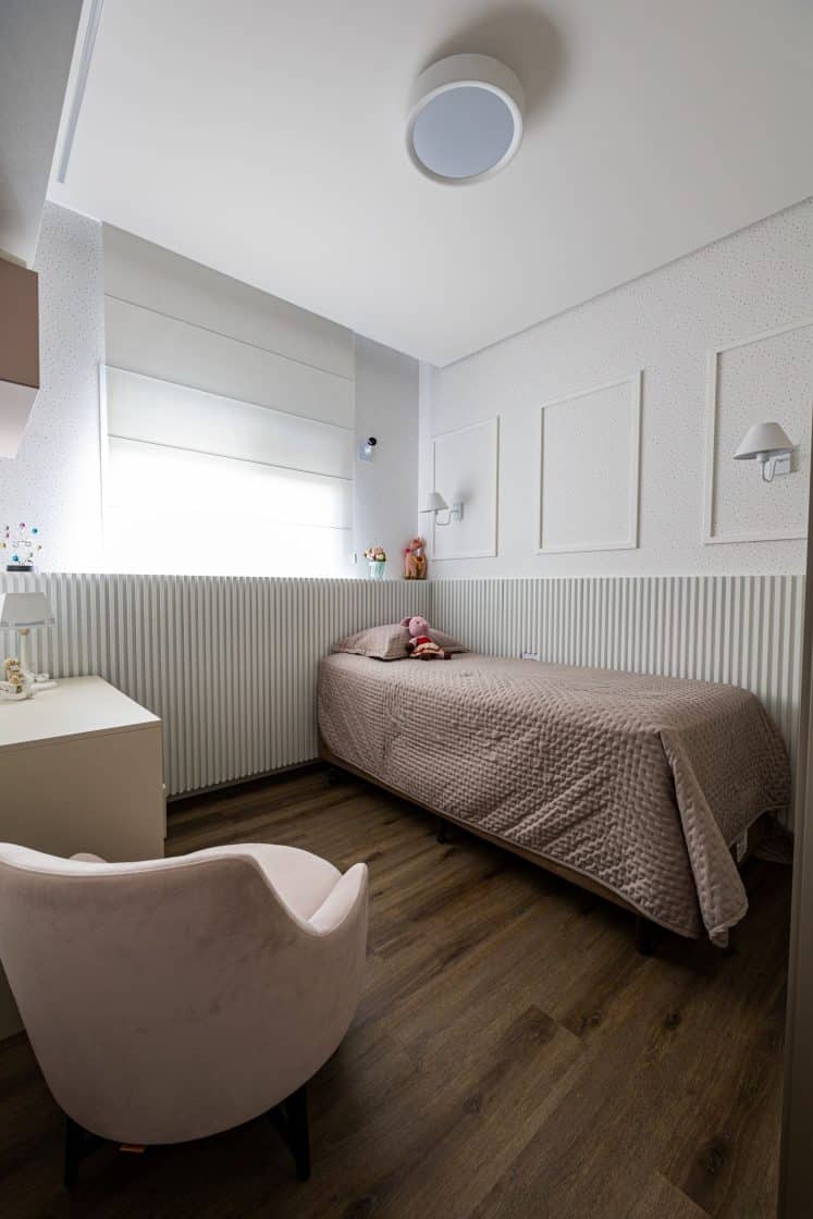 quarto para criança com roupa de cama cor de rosa, piso de madeira e poltrona aveludada
