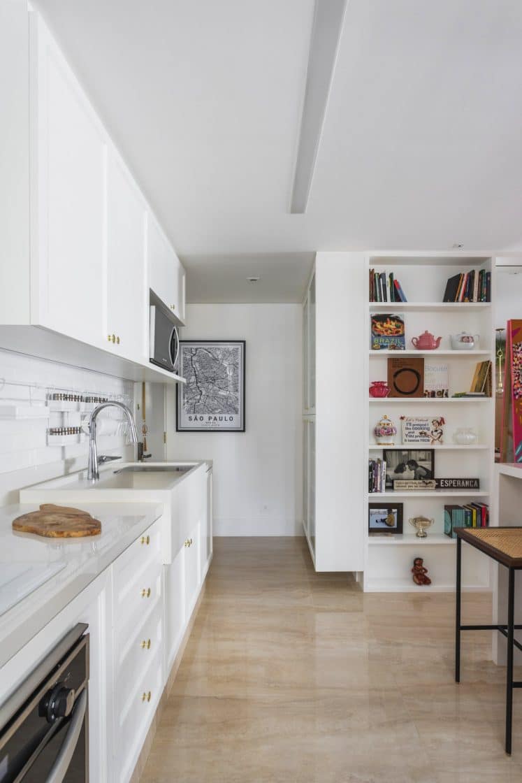 cozinha branca, bancada de preparo branca, quadro ao fundo, na parede, e praleteira com livros