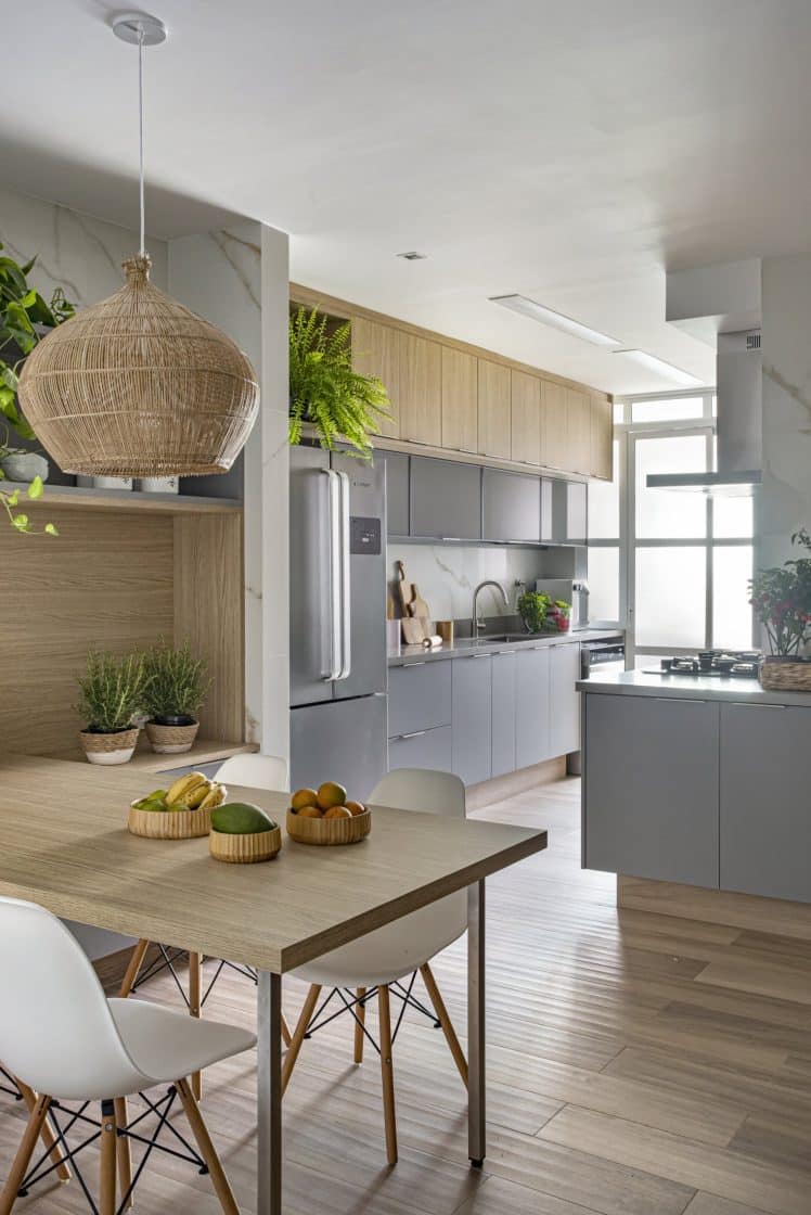 Cozinha com armários de cor cinza, mesa em madeira e plantinhas e ervas sobre móveis 