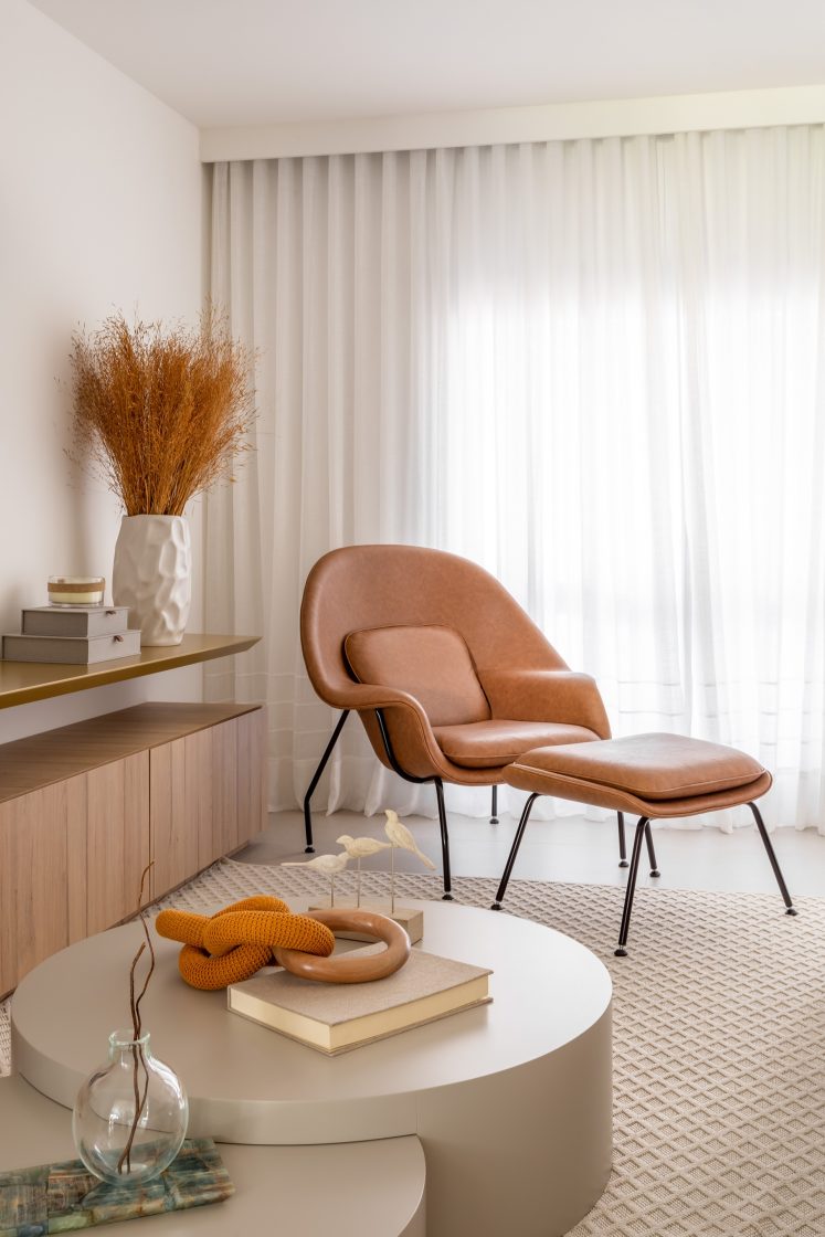 Sala de estar com poltrona com descanso para pés em couro caramelo, mesa de centro com decorações combinando com as cores da sala