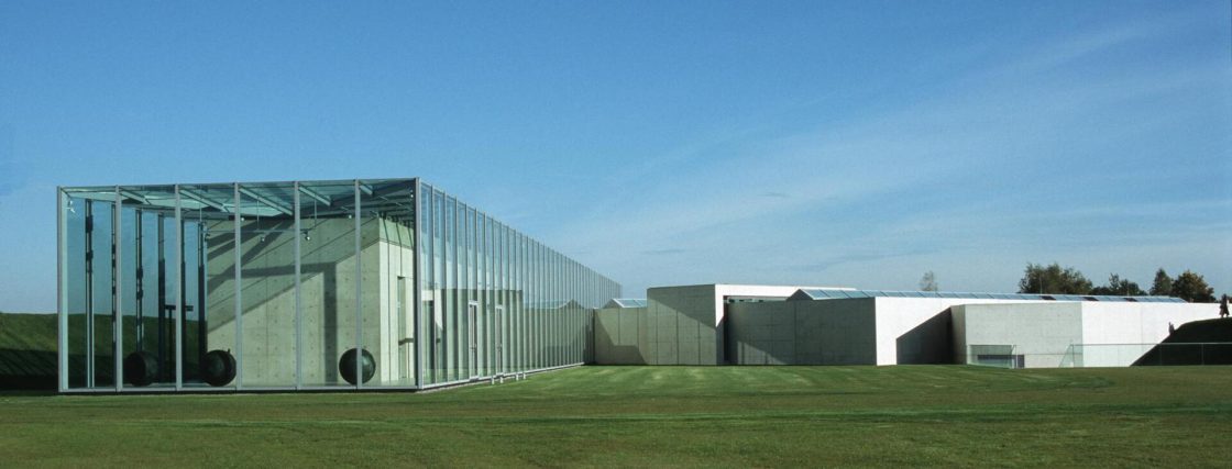 Foto do Museu Langenn Foundation em Neuss, Alemanha. Edificação em vidro e concreto, com gramado ao redor.