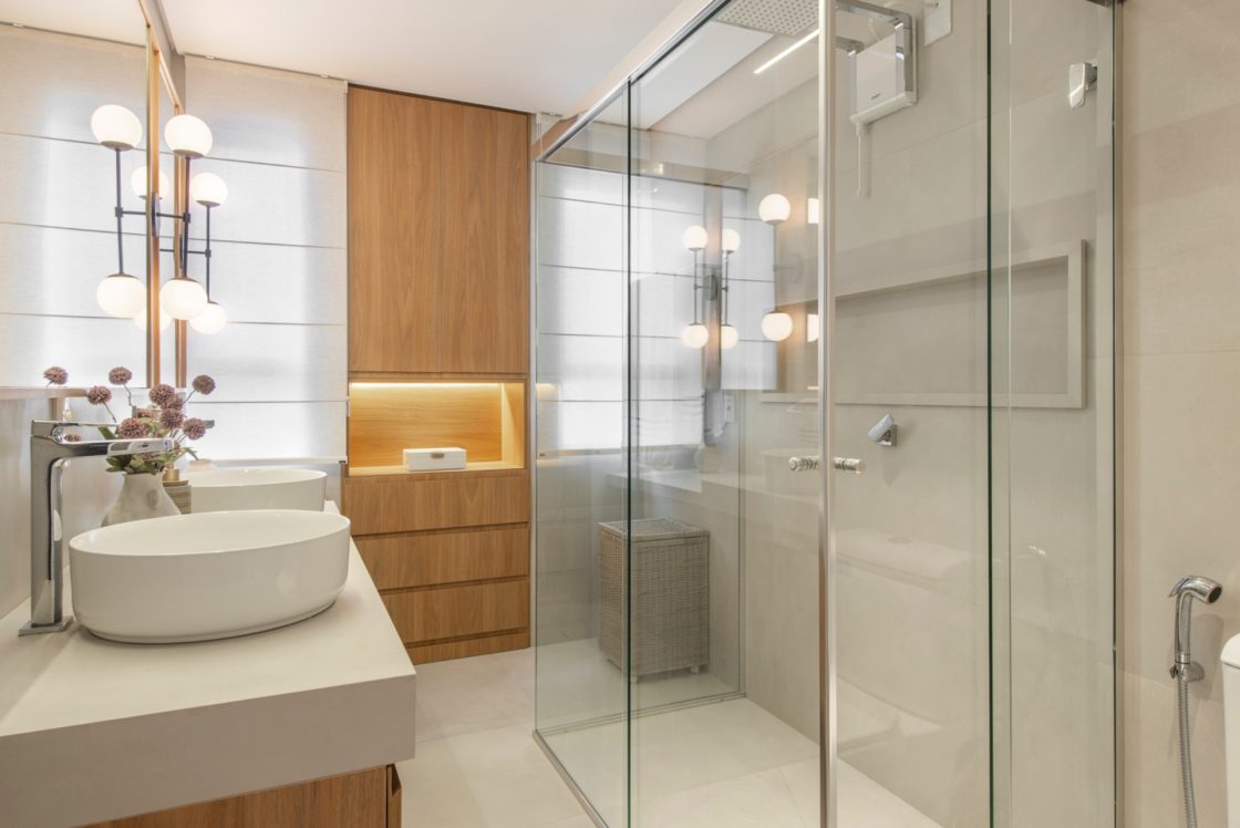 Banheiro em tons claros com destaque em madeira. Box com nicho de mármore branco.