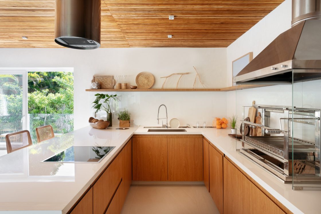 Cozinha com piso e bancadas claras, além de armários e teto de madeira