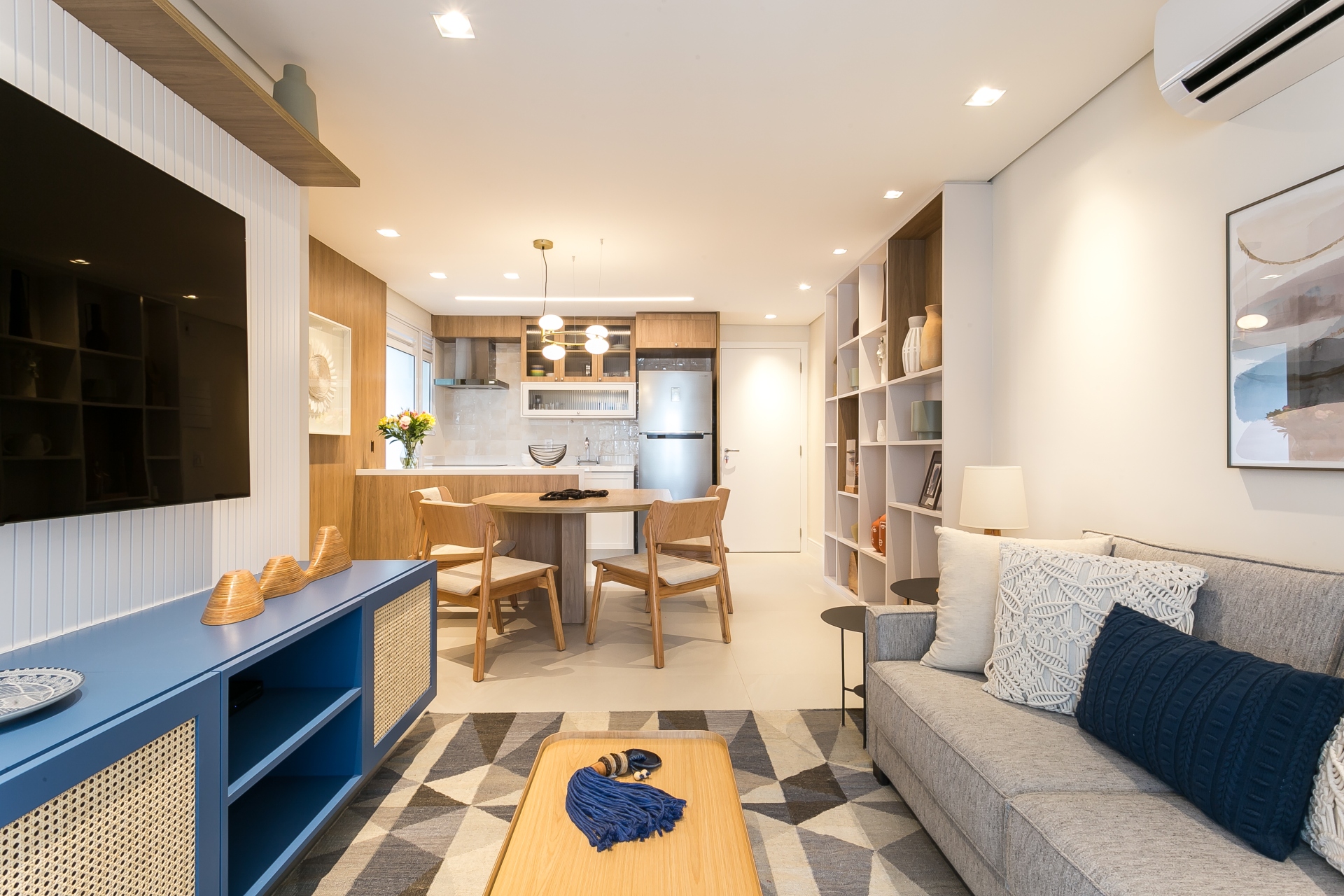 Apartamento com conceito aberto, integrando sala e cozinha, em tons claros e poucos elementos em azul que se destacam