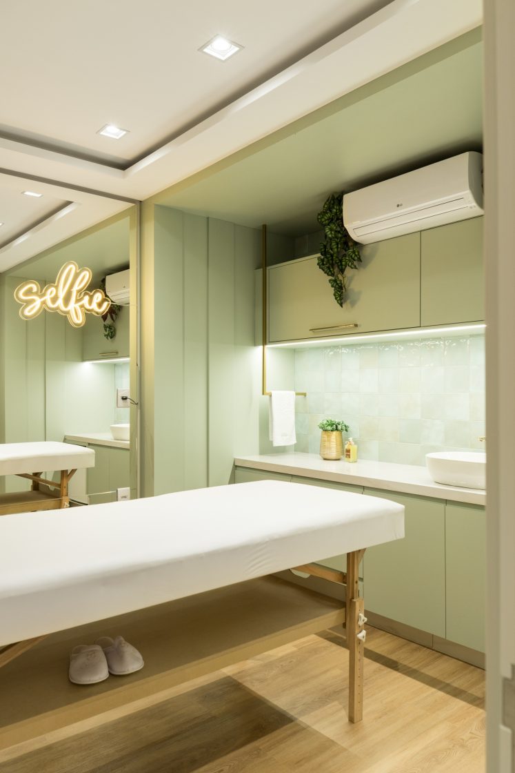 Sala de massagem clean com azulejos com acabamento brilhoso, armários em verde claro e detalhes em dourado 