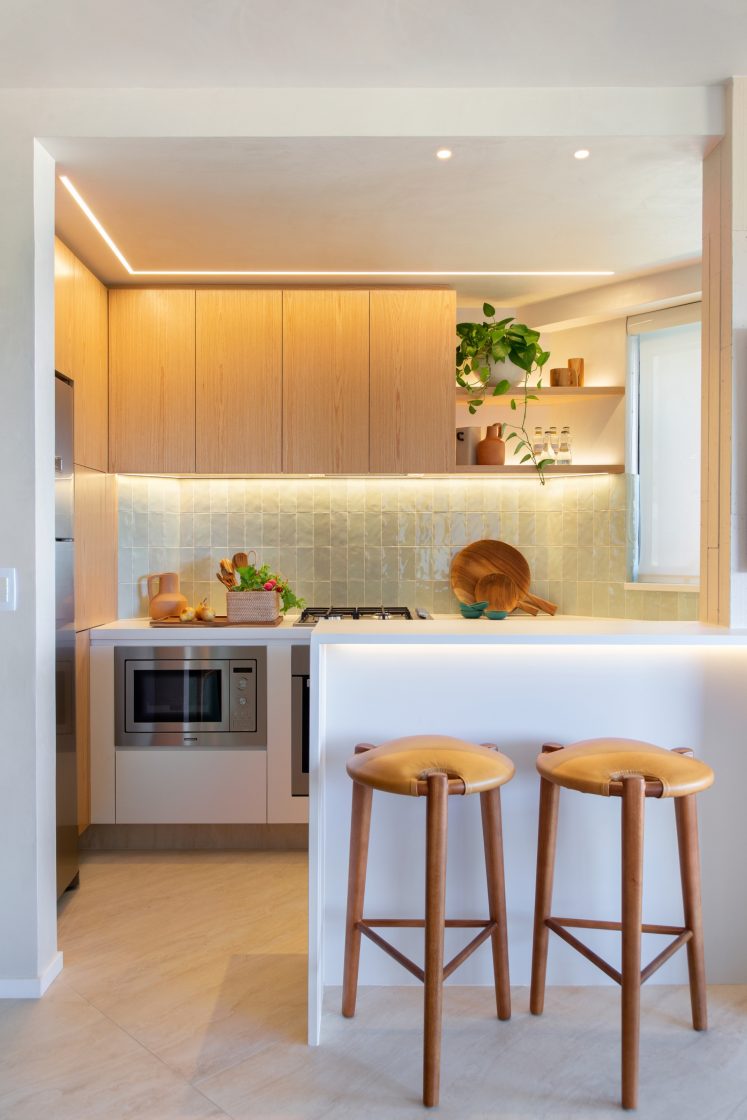 Cozinha pequena com moveis em madeira clara  bancada branca e paredes em azulejos com acabamento brilhoso