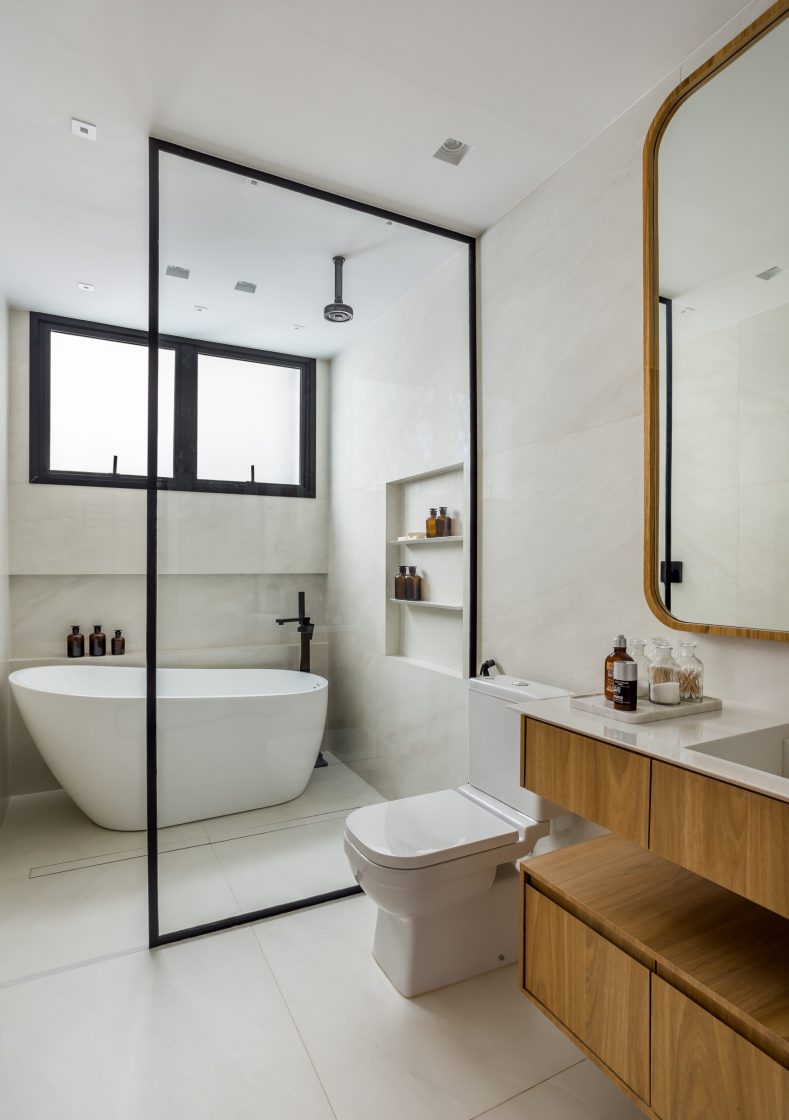 Banheiro iluminado em tons de branco, mármore branco e detalhes em preto e gabinete em madeira