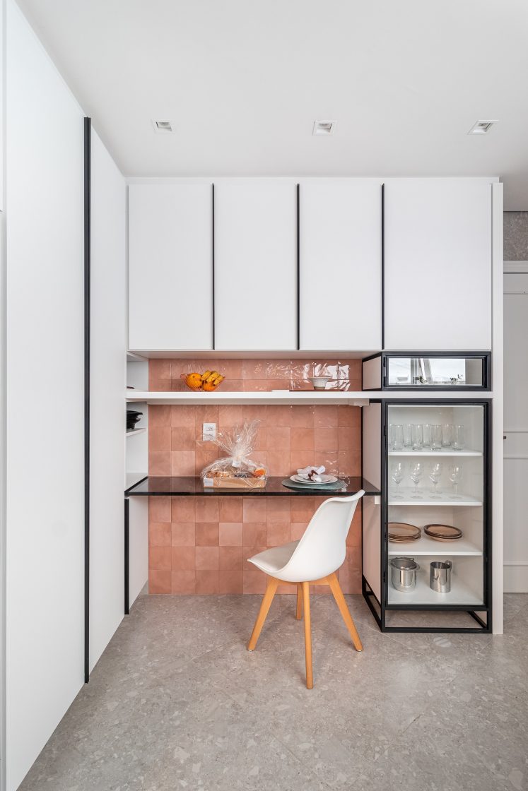 Cozinha com armários em branco e detalhes em preto com parede em azulejo rosa com acabamento brilhante