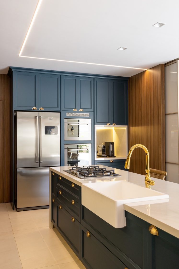 Cozinha intimista em tons de azul para os armários embutidos e detalhes em dourado. Bancada em ilha com fogão e pedra de mármore claro