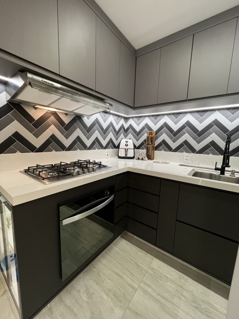 Cozinha com armários cinza-escuro e cinza-claro, bancada branca e backsplash geométrico