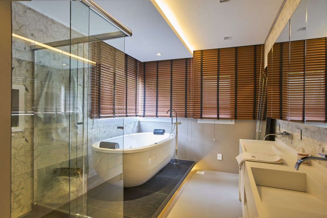 Banheiro com box para ducha separado da banheira e janelas com persianas para criar um aconchego 