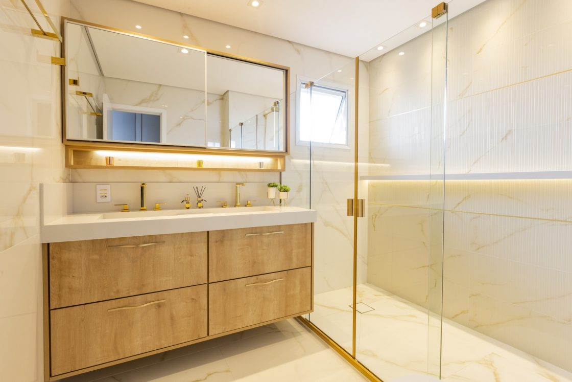 Banheiro em mármore claro com detalhes em dourado e gabinete duplo
