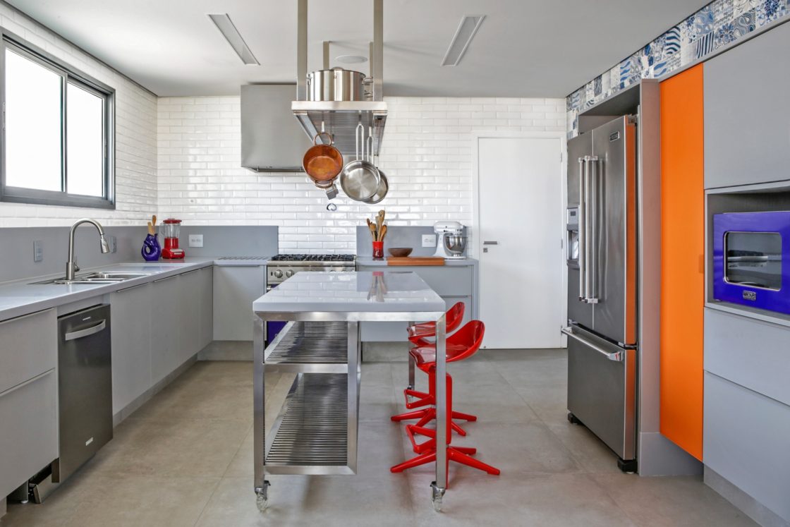 Cozinha com pegada industrial em tons cinza e pequenos detalhes com cor, como banquetas, forno