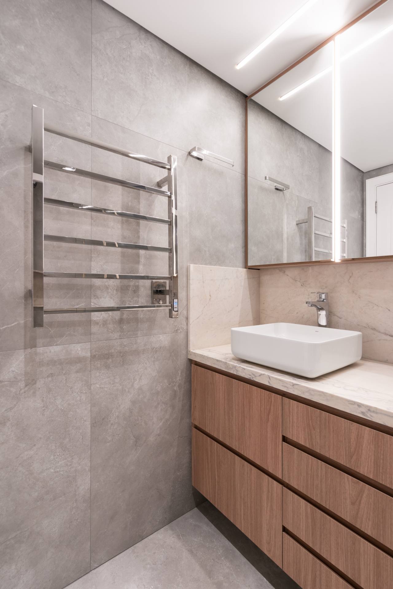 Banheiro minimalista com detalhes em cinza e madeira, toalheiro térmico prata