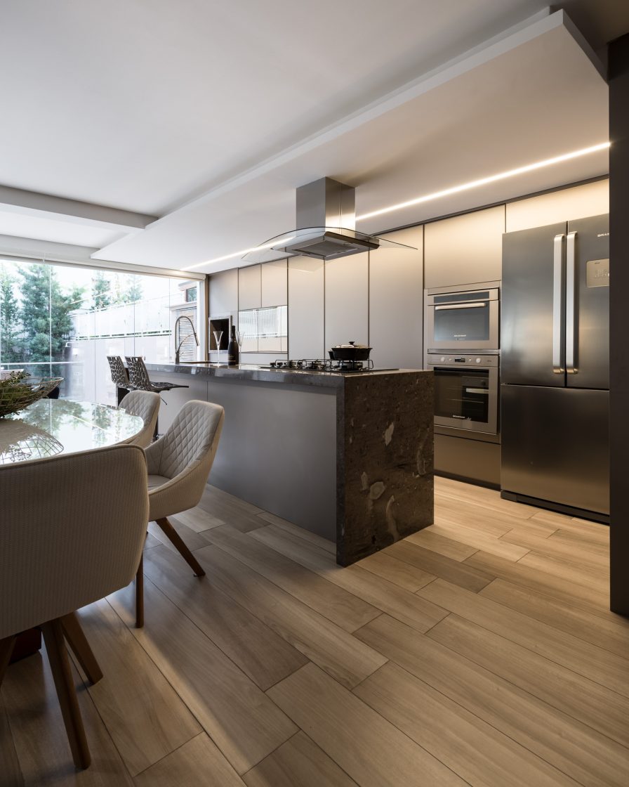 Cozinha gourmet com bancada cinza, piso em madeira e iluminação linear em led