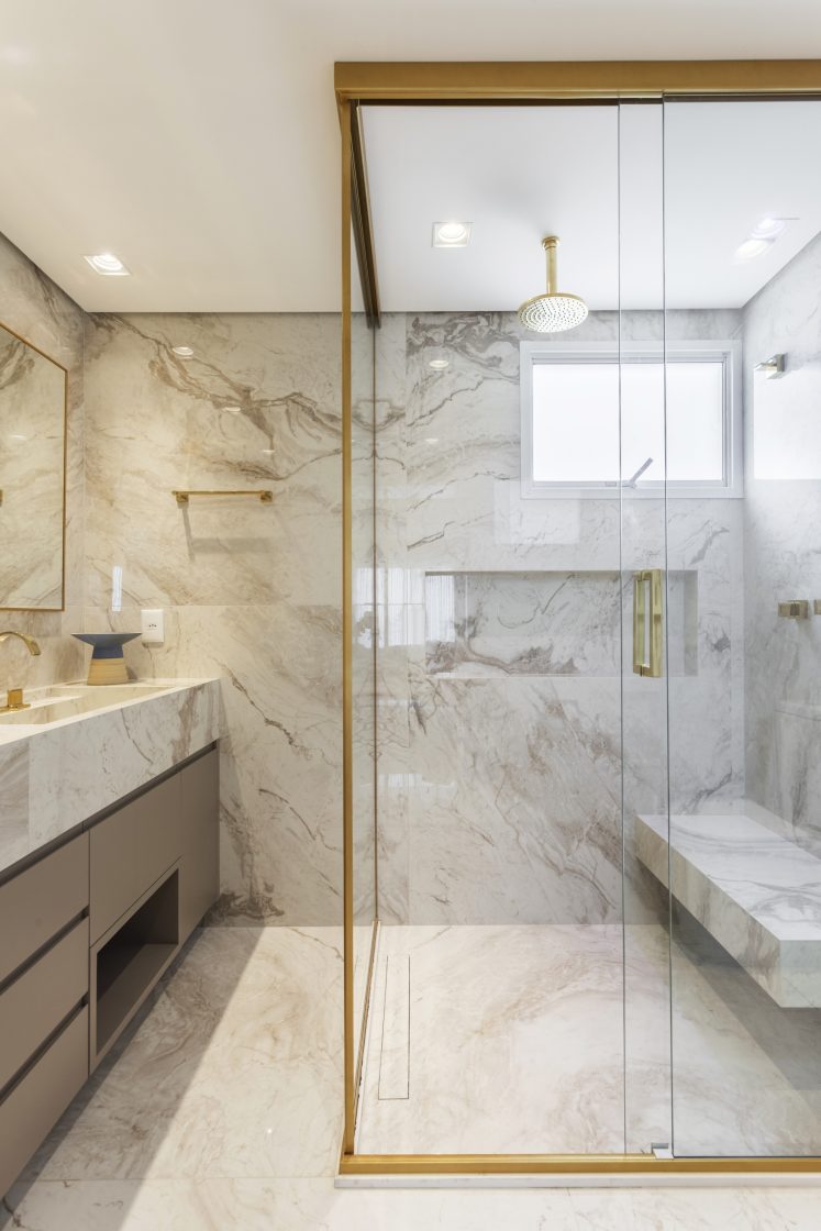 Banheiro em pedra de mármore com box amplo e banco em pedra com detalhes em dourado