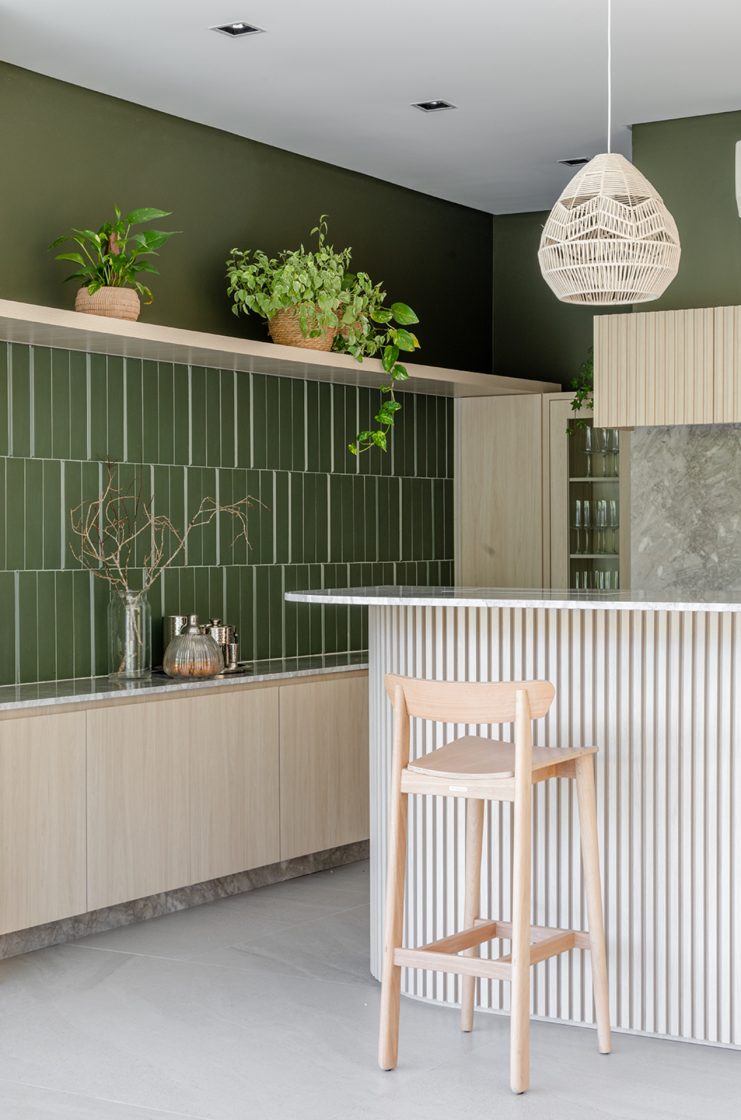 Cozinha verde e bege com elementos em madeira e planta jiboia e outras espécies de planta
