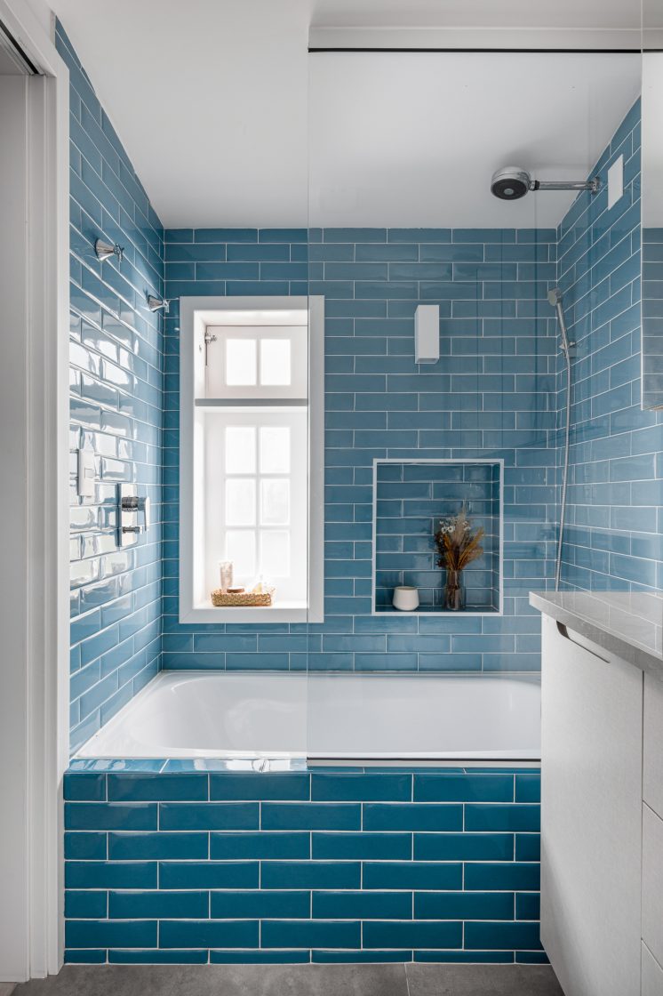 Banheiro com azulejos em azul nas paredes do box e banheira, com nicho em forma de quadrado