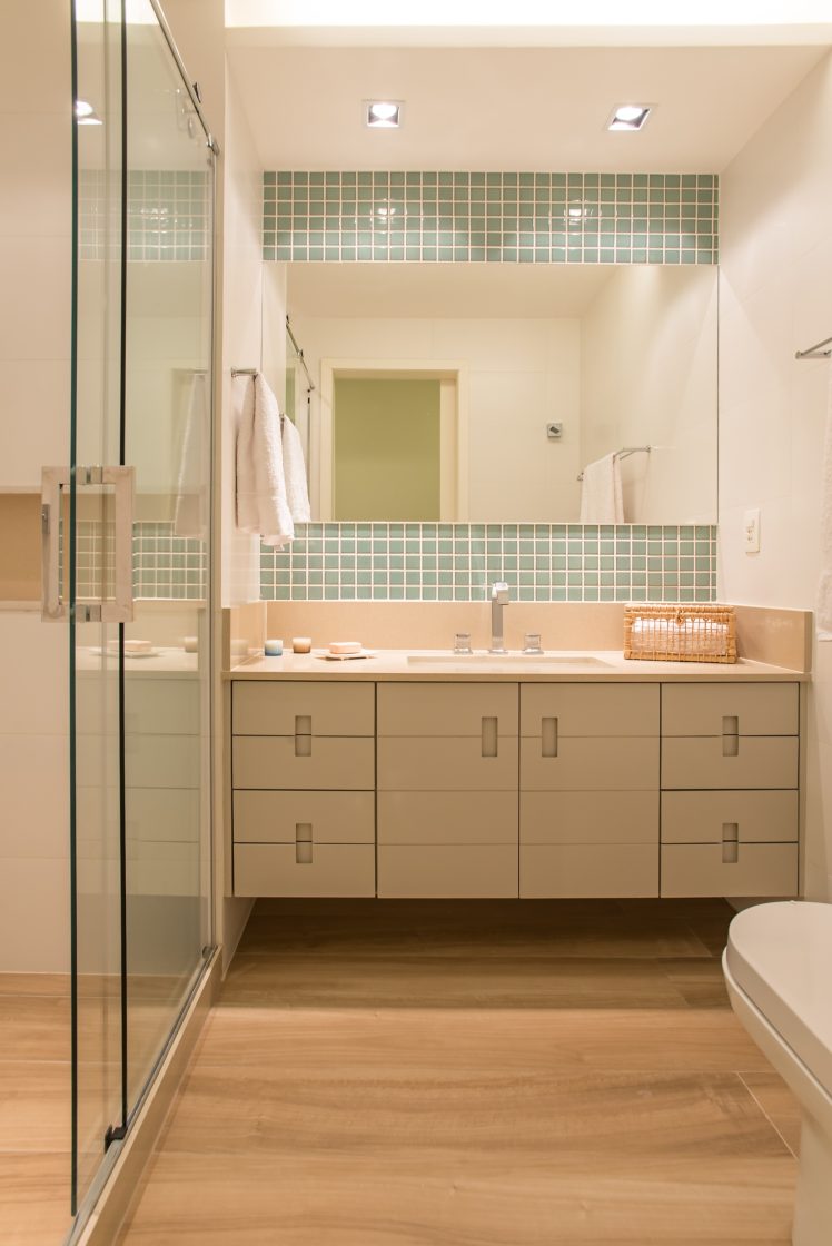 Banheiro em tons claros, iluminado, com amplo gabinete e detalhe com pastilha colorida