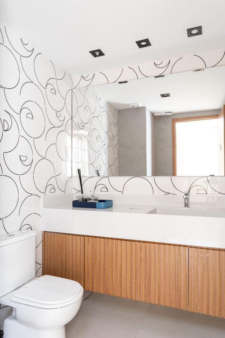 Banheiro com com gabinete em madeira e papel de parede com padrões geométricos  