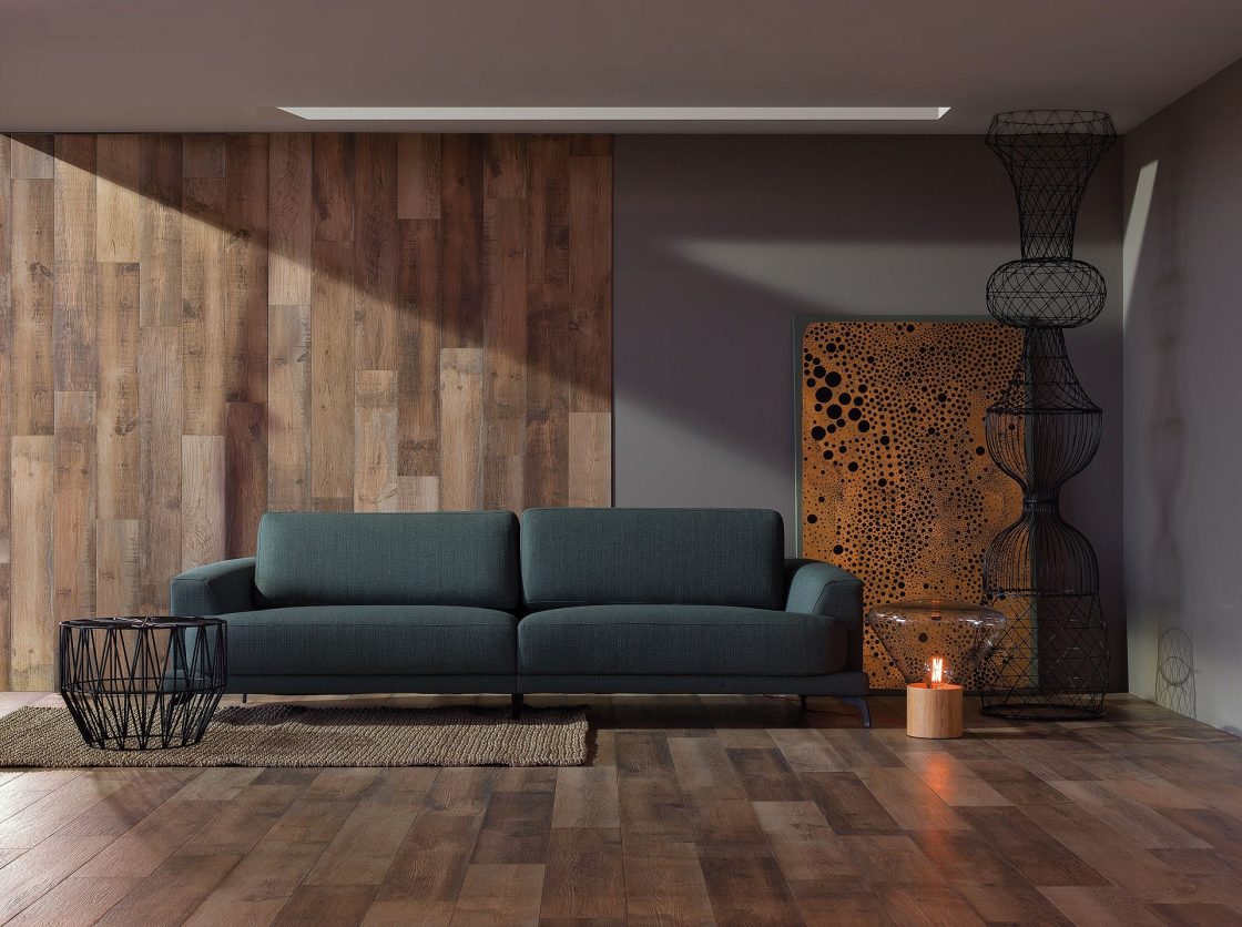 Sala com piso e parede de madeira, sofá verde, quadros e objetos decorativos escuros