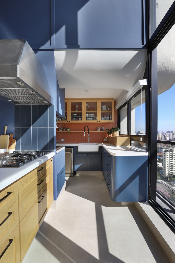 Cozinha azul e laranja em apartamento, com grandes janelas e luz natural